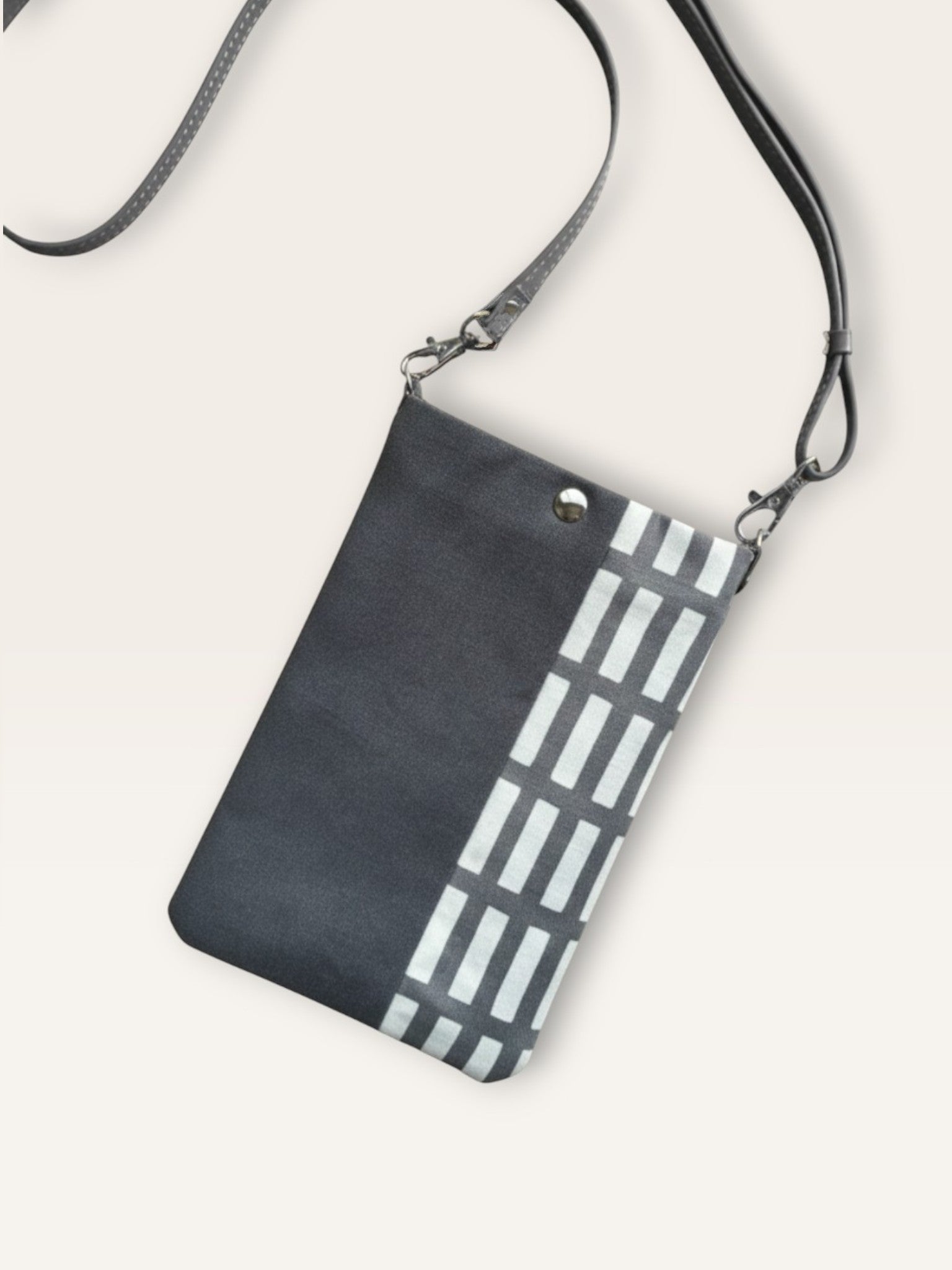 A grey canvas phone bag with a vertical panel of white rectangular stripes on the right side. The bag includes a thin grey crossbody strap.
