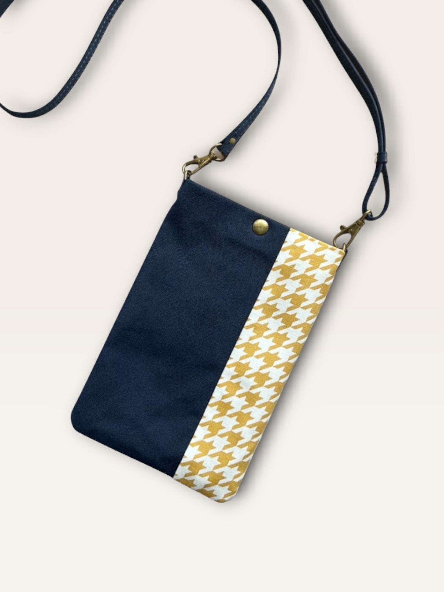 A slim handmade phone bag featuring a navy blue canvas panel and a mustard yellow and white houndstooth pattern. Includes a navy adjustable strap.
