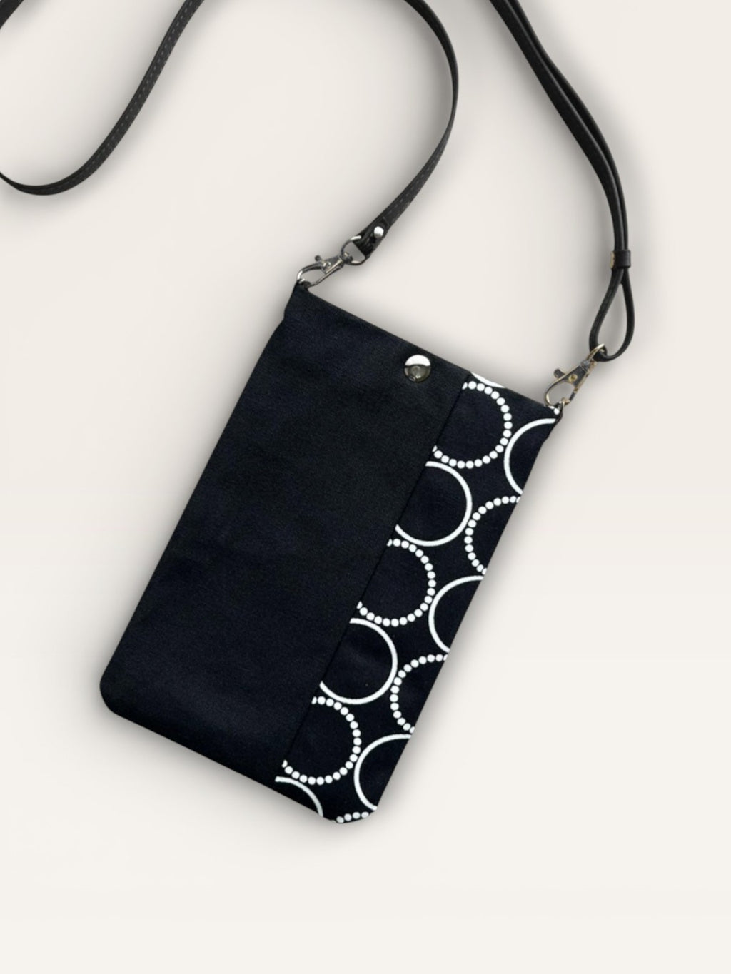 vertical fabric phone pouch with a black left panel and a white circle pattern on a black background on the right. It has a matching black strap and silver hardware.